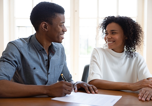 man and woman looking at once another smiling with a document in front of them