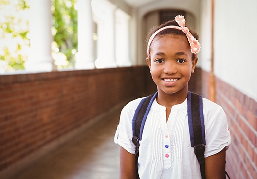 young girl with her backpack standing in the school hall