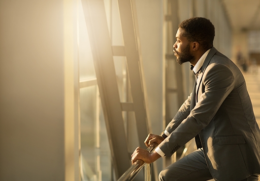 man standing, with his hands on a railing looking outside the office building window